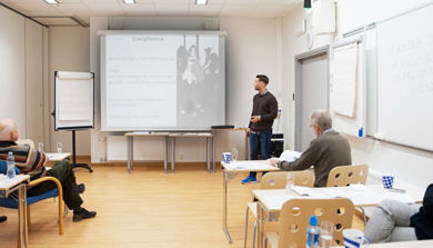Kursholder foreleser med presentasjon på lerret i lokale med flere kursdeltakere i klasseromsetting. Foto